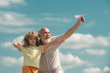 Grandfather and grandson playing with paper plane against summer sky background. Child boy with dreams of flying or traveling.