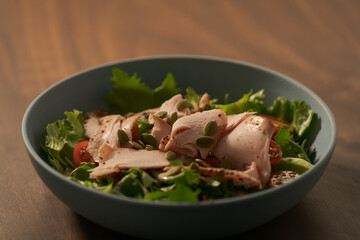Salad with roasted turkey and cherry tomatoes decorated with pumpkin seeds in blue bowl