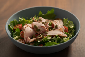 Salad with roasted turkey and cherry tomatoes decorated with pumpkin seeds in blue bowl