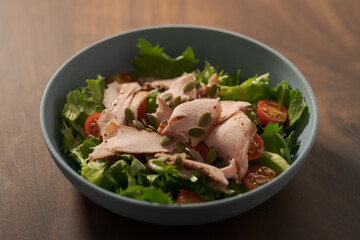 Salad with roasted turkey and cherry tomatoes decorated with pumpkin seeds in blue bowl