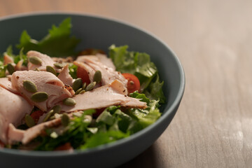 Salad with roasted turkey and cherry tomatoes decorated with pumpkin seeds in blue bowl