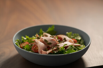 Salad with roasted turkey and cherry tomatoes decorated with pumpkin seeds in blue bowl