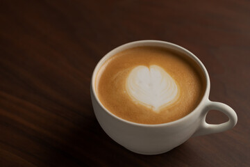 Flat white in white cup with simple latte art on walnut wood table