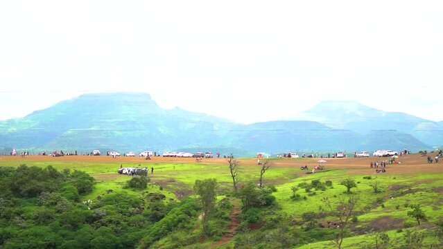 View of the Sahyadri Mountain range with cars of tourists in front of it as seen from the Saputara Table Point at Saputara in Gujarat, India. Tourists park their cars and enjoy the view of green hills
