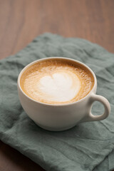 Flat white in white cup with simple latte art on walnut wood table with turquoise napkin