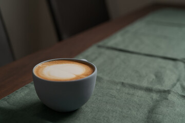 Flat white in white cup with simple latte art on walnut wood table with turquoise napkin