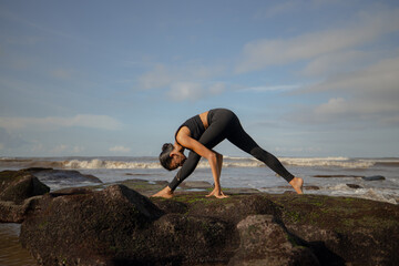 Slim Asian woman practicing yoga on the beach. Standing pose Trikonasana Parivrtta. Revolved Triangle Pose. Strong flexible body. Yoga retreat in Bali. Sport lifestyle. Mengening beach