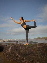 Outdoor morning yoga. Asian woman standing on the rock in Natarajasana, Lord of the Dance Pose. Balancing, back bending asana. Exercise on the beach. Copy space. Mengening beach, Bali