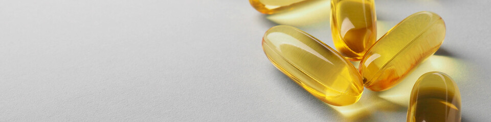 Fish oil. Yellow softgels or capsules lie on a white or light gray surface. Vitamins and a healthy lifestyle. Banner or headline. Softgel close-up. Omega-3 fatty acids. Macro