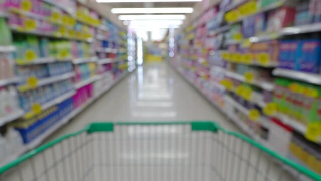 Blurry video of empty supermarket cart moving forward in store for buy some goods and products on the left and right hand shelf.