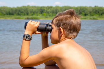 boy looking through binoculars on the river bank
