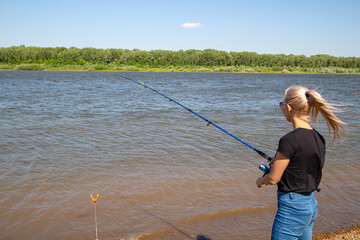 girl with a fishing rod on the river bank on a warm summer day
