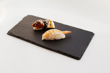 Nigiri and unagi Sushi japan food on black board plate with wooden chopsticks isolated on white. Sashimi sushi snacks and chopsticks japanese food with fish and seafood isolated on white close up.