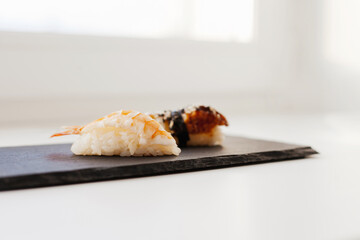 Nigiri and unagi Sushi japan food on black board plate with wooden chopsticks isolated on white. Sashimi sushi snacks and chopsticks japanese food with fish and seafood isolated on white close up.