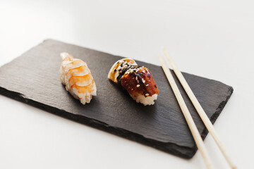 Nigiri and unagi Sushi japan food on black board plate with wooden chopsticks isolated on white. Nigiri unagi sushi and chopsticks japanese food isolated on white closeup.