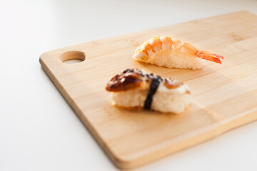 Fototapeta na wymiar Sushi delivery and takeout - Nigiri and unagi sushi japanese food on wooden board isolated on white. Nigiri unagi sushi and chopsticks japanese food on wooden board close up.