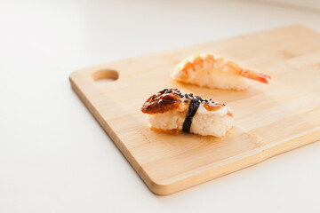 Sushi delivery and takeout - Nigiri and unagi sushi japanese food on wooden board isolated on white. Nigiri unagi sushi and chopsticks japanese food on wooden board close up.