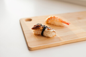 Sushi delivery and takeout - Nigiri and unagi sushi japanese food on wooden board isolated on white. Nigiri unagi sushi and chopsticks japanese food on wooden board close up.
