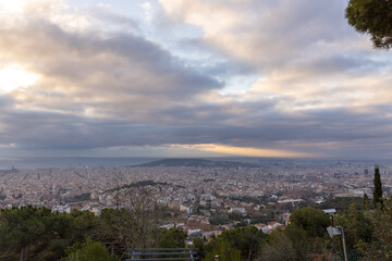 Picturesque landscape of Barcelona from the hill in the early morning. Sunbeams through the clouds. Dramatic sky over the city. Autumn in Barcelona, Spain.