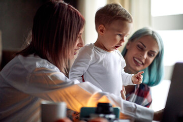 A young lesbian couple playing at home with their adopted son. Family, kid, parents, lgbt