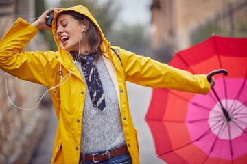 Close-up of a young cheerful woman in a yellow raincoat who is enjoying while listening to the...