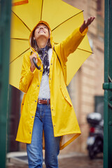 A young cheerful woman with a yellow raincoat and umbrella who is enjoying the rain while walking...