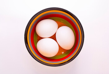 Three white chicken eggs in a colored deep bowl