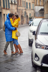 A young couple in love is standing on the street in the hug and kissing while walking the city on a cloudy day. Walk, rain, city, relationship