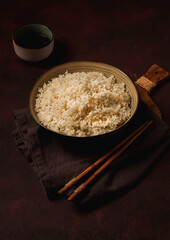 A plate of boiled rice, with wooden sticks, on a brown background, no people, selective focus, toned.