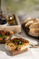 Ciabatta bread sandwich with humus and dried tomatoes, arugula leaves on white table. Italian traditional food - bruschetta, antipasto. with ingredients. Copy space. 