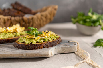 Avocado and egg sandwich with whole grain brown bread and greens, healthy diet vegan food. Breakfast on wooden board, white table. Copy space.