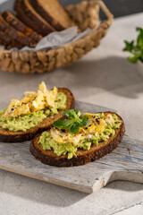 Avocado and egg sandwich with whole grain brown bread and greens, healthy diet vegan food. Breakfast on wooden board, white table. Copy space.