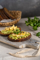 Avocado and egg sandwich with whole grain brown bread and greens, healthy diet vegan food. Breakfast on wooden board, white table. Copy space.