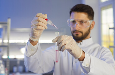 Man observes the interaction of components. Close up of a test tube with liquid in the hands of a...