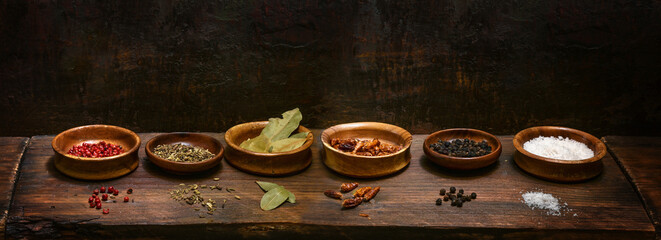 Small bowls with dried spices on a dark rustic wooden plank, cooking and food concept, panoramic...