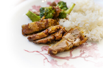 Slices from crispy fried duck breast with broccoli and rice in a spicy sauce on a white plate with Asian decoration, tasty Chinese dish, copy space, selected focus