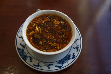 Chinese spicy and sour soup in a white porcelain bowl with Asian pattern on a dark brown table, copy space, selected focus