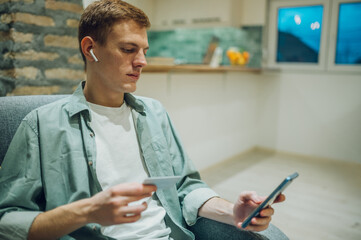 Redhead man shopping online with credit card and a smartphone at home