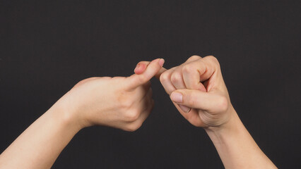 Pinky promise or pinky swear hand sign on black background.
