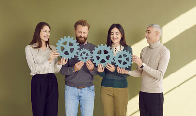 Corporate community. Portrait of four people holding and connecting turquoise wooden gears that...
