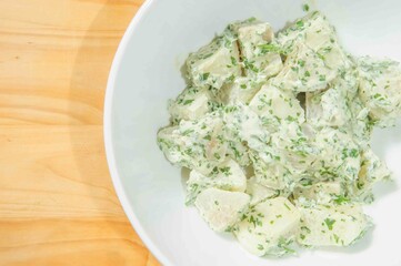 Potato salad with fresh dill and green onion on a rustic wooden table.