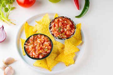Salsa sauce and nacho chips on white plate. Mexican homemade salsa dip and ingredients on a white background. Copy space. Top view