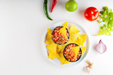 Salsa sauce and nacho chips on white plate. Mexican homemade salsa dip and ingredients on a white...