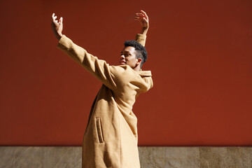 Young black man dancing on red urban wall.