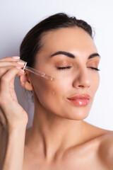 Fototapeta premium Close beauty portrait of topless woman with perfect skin and natural make-up, holds serum for youth and skin hydration, dropper with cosmetic oil.