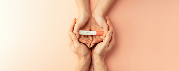 Pregnancy test kit. Female hand hold positive pregnant test with silk ribbon on pink banner...