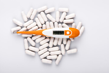 Electronic thermometer and pills on white background