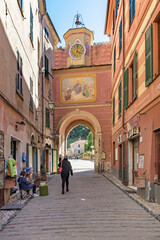 Finalborgo, Finale Ligure, Italy. May 5, 2021. View of Porta Testa with the Clock Tower seen from the narrow street Via Giovanni Nicotera.