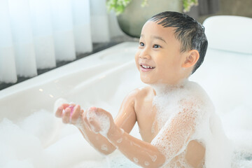 smiling happy asian child boy is playing with white foam in tub bath at home.