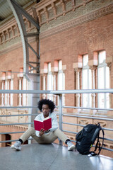 African American man with afro hairstyle and casual clothes reading a book at train station. Travel and lifestyle concept. Space for text.